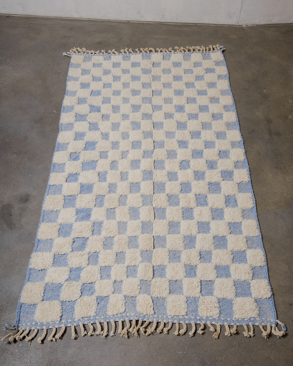 Checkered rug with blue and beige pattern on a concrete floor